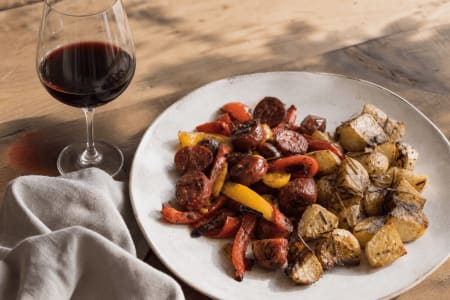 Gegrillte Chorizo mit roter und gelber Paprika sowie Rosmarinkartoffeln, serviert mit einem Glas Ramón Bilbao Crianza als passende Speisebegleitung.