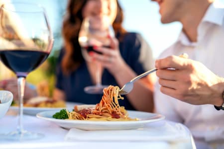 Ein Paar isst von einem Teller Spaghetti Napoli mit einem Glas Rotwein.