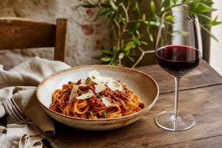 Pasta al Ragù mit einem Glas Rotwein in mediterranem Ambiente.
