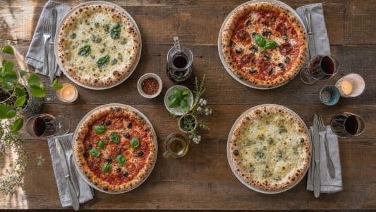Vier Pizzen und Rotweingläser auf einem Esstisch.