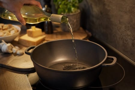 Weißwein wird in einen Fonduetopf auf der Küchenzeile gegossen.