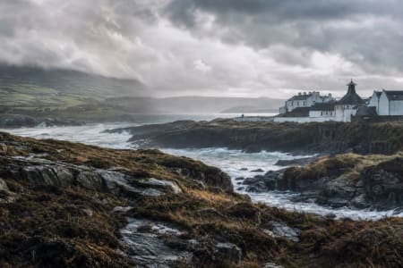 Bergige Landschaft mit Fluss und Brennerei-Gebäude auf der schottischen Insel Islay.