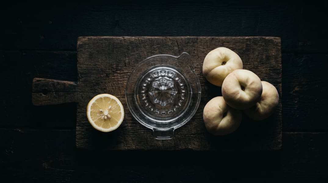 Halbe Zitrone, Pfirsiche und Saftpresse auf einem Holzbrett.