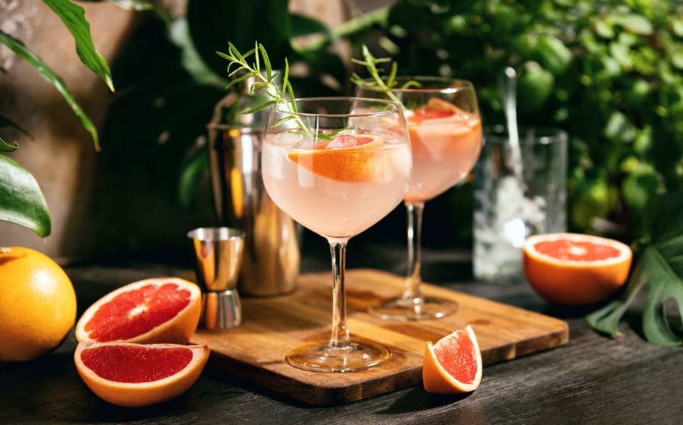 Zwei leicht pinke Cocktails und Grapefruit-Stücke auf Holzbrett.
