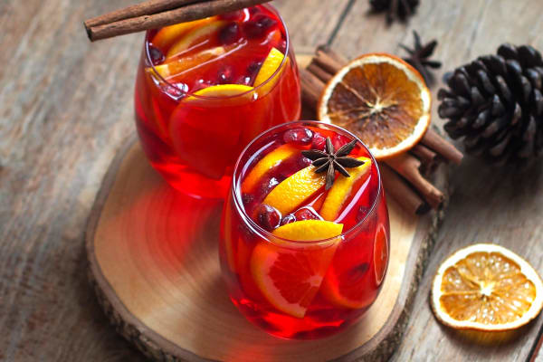 Zwei Winter-Ruby-Cocktails, mit Zimtstangen und Orangenscheiben garniert.