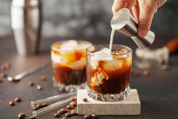 Zwei Gläser White-Russian-Cocktail werden mit Sahne zubereitet.