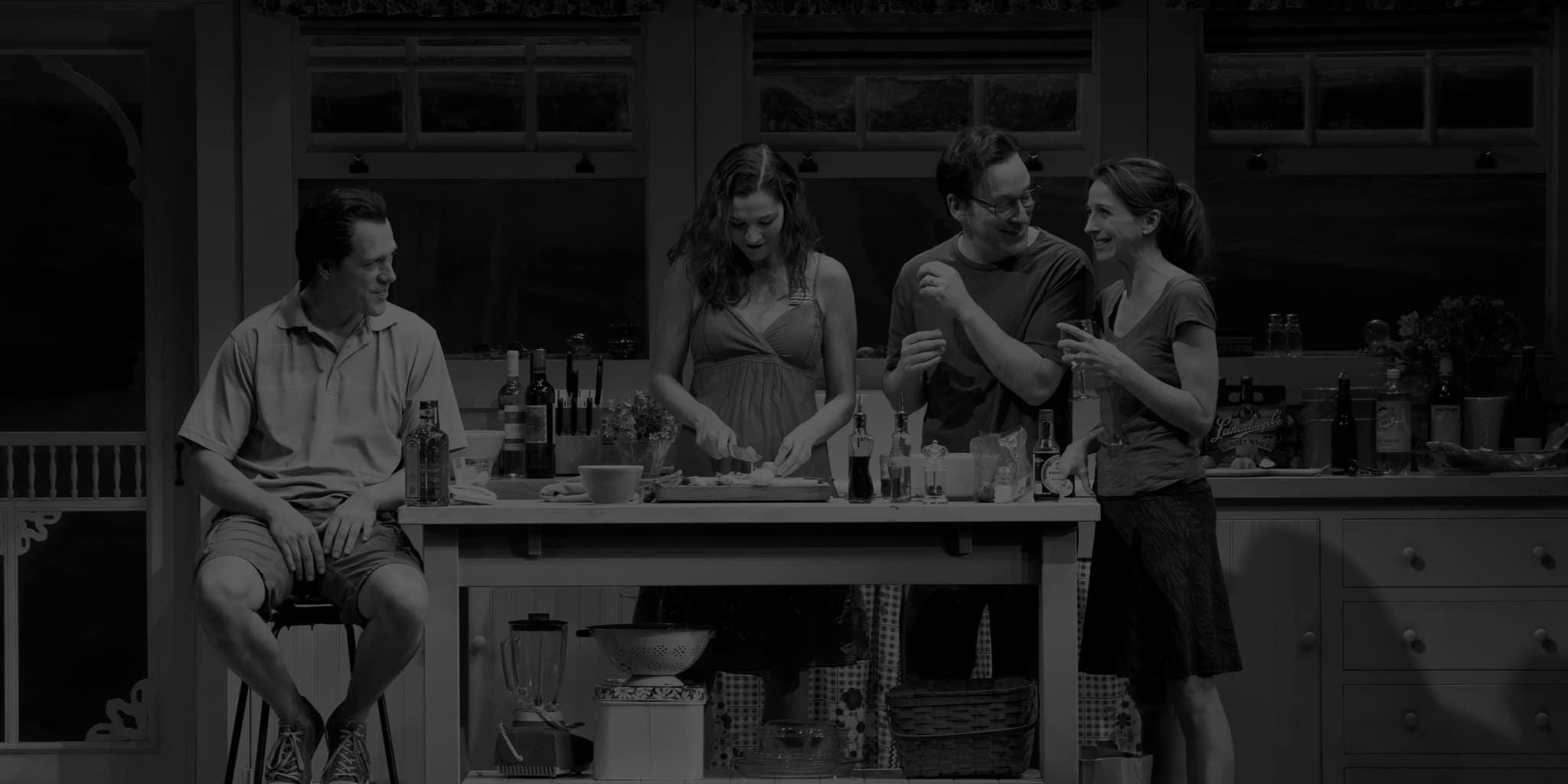 Production image from DINNER WITH FRIENDS. Two men and two women sit and stand around a kitchen island, preparing dinner.