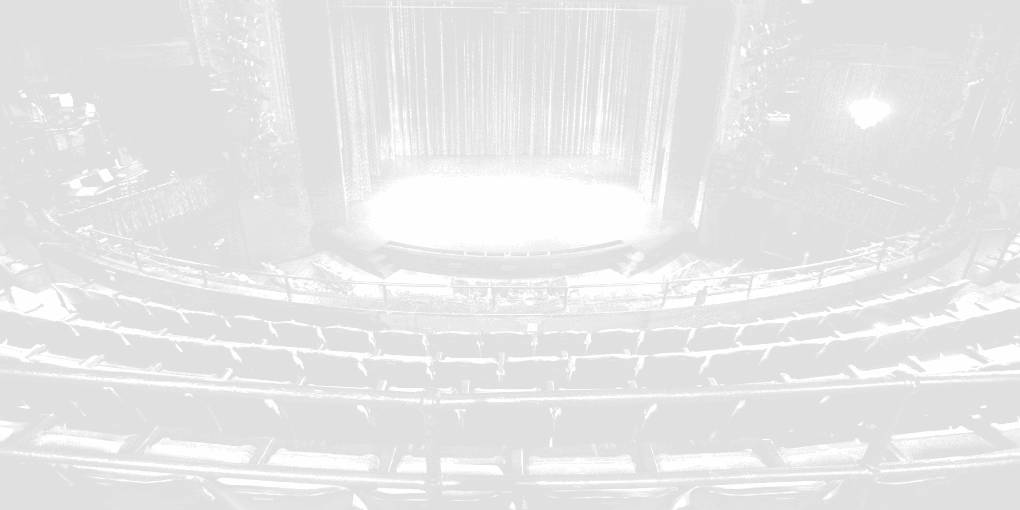 A faded black and white image of an empty stage and audience.