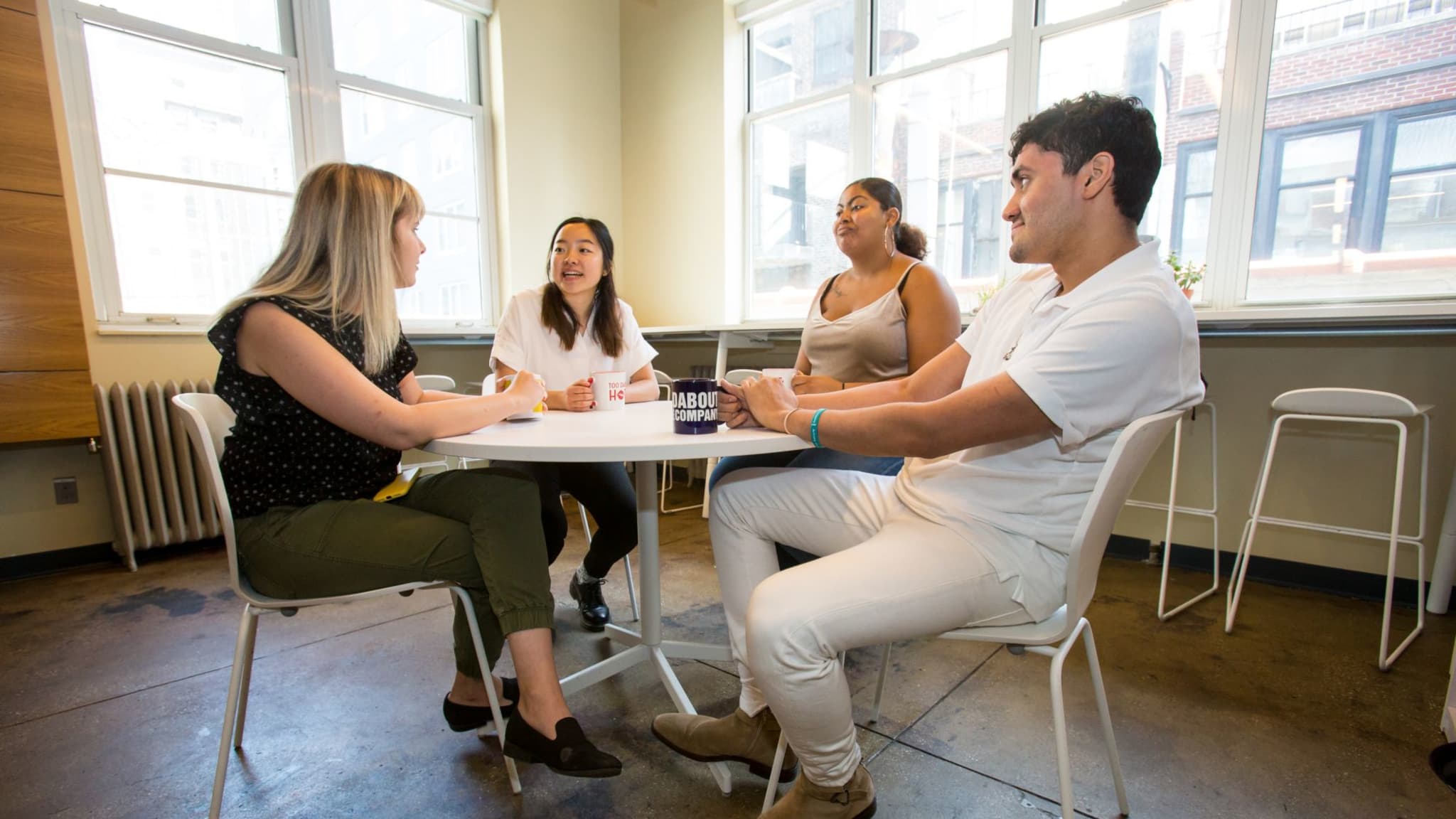 Several Intens sitting at a table in a bright room laughing and having a conversation. 