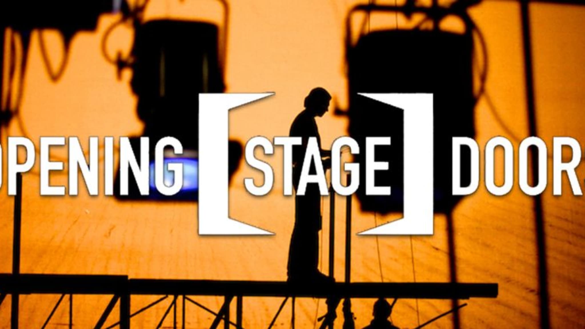 Opening Stage Doors. A silhouette of a person standing on a platform surrounded by theatre lights. The background silhouetting them is orange.