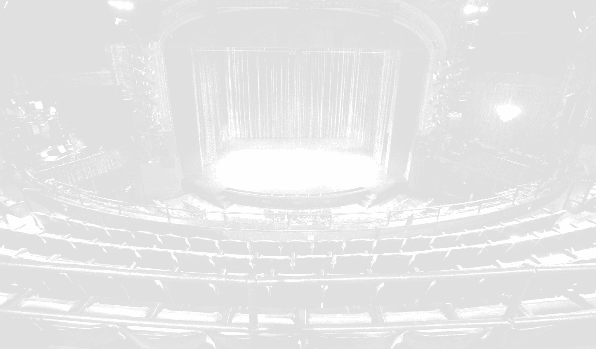 A faded black and white image of an empty stage and audience.