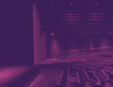 The empty house of the Laura Pels Theatre. Rows of grey chairs incline upwards towards the back of the house.