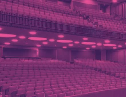 The empty house of the Stephen Sondheim Theatre. The seats are bright orange and the walls are a dark grey.