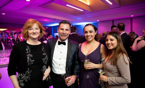 Four people in fancy attire hold wine glasses and pose for a photo at an event.