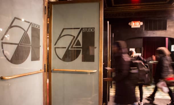 The doors to Studio 54 as people enter. A large, decorative 54 sits in the center of the foggy glass doors.