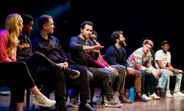 A group of actors from HOLIDAY INN sit on chairs at the front of the stage and hold microphones as they speak to the audience.