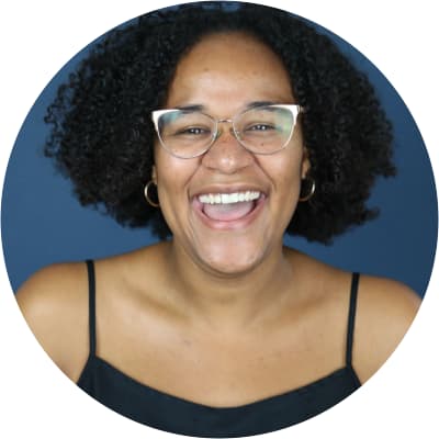 A mid-laugh Vivian J. O. Barns, who has a medium skin tone, very curly textured black hair, freckles, glasses, earrings, and a black tank top.