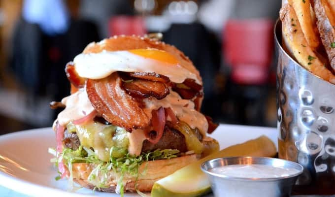 A stacked double burger with bacon, a pickle slice, and fries and ranch dressing.