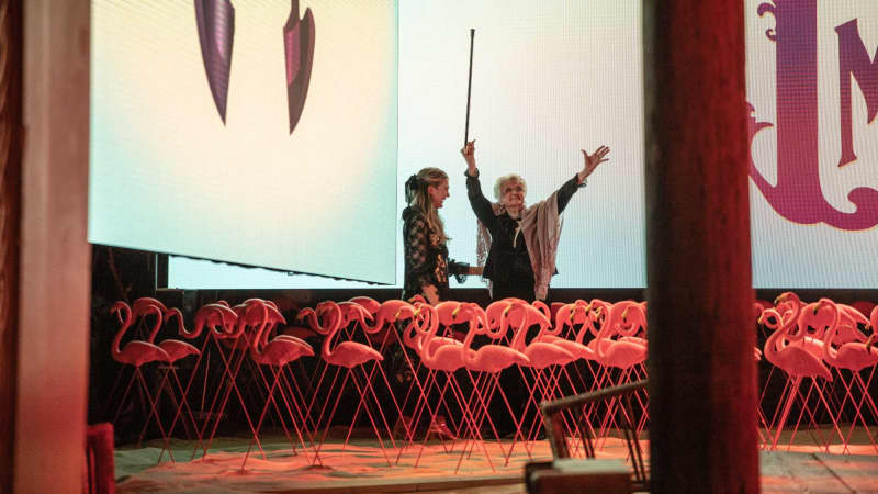 Lily Rabe and Angela Landsbury, who holds her arms up while holding a can, stand on stage behind a bunch of pink flamingo lawn decorations from THE ROSE TATTOO.