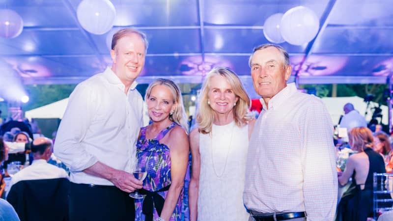 A group of four people in formal attire pose for a photo under an outdoor pavillion lit with purple lighting.