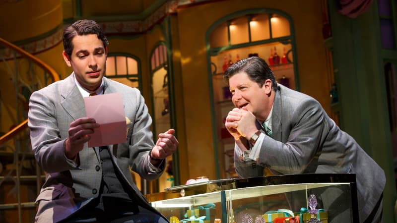 Michael McGrath leans over a perfume counter while Zachary Levi reads a letter in SHE LOVES ME.