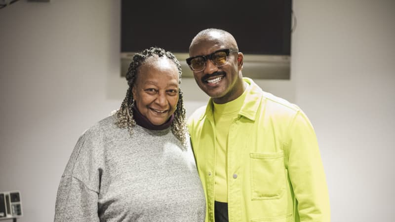 Two dark skinned individuals, one man and one woman, smiling and posing for a picture with their arms around each other. 