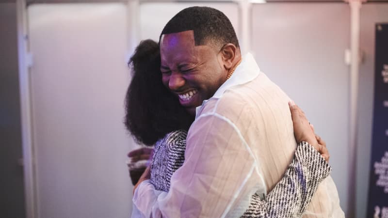 One man and one woman both with dark skin hugging each other and smiling. 