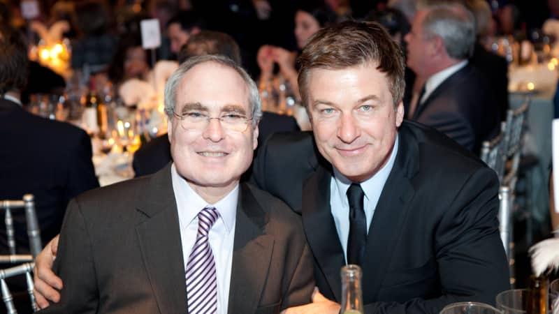 Todd Haimes and Alec Baldwin lean in for a photo at a formal dining table.