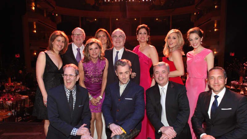 A group of people in formal attire clump together for a group photo in a ballroom.