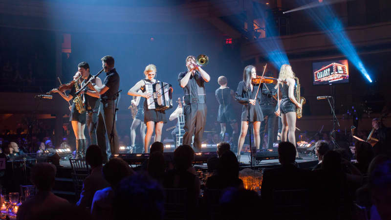 A group of performers from CABARET play a variety of instruments on stage, including the violin, trumpet, accordion, and saxophone.