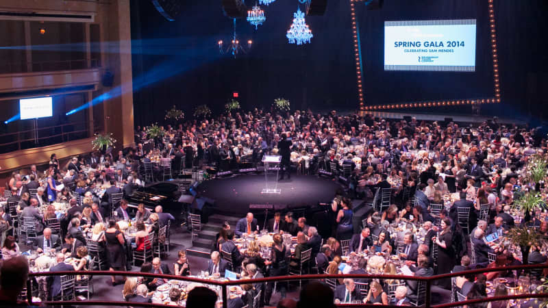 A wideshot of the 2014 gala at the Hammerstein Ballroom. Round fancy dining tables surround a round stage in the middle of the room.