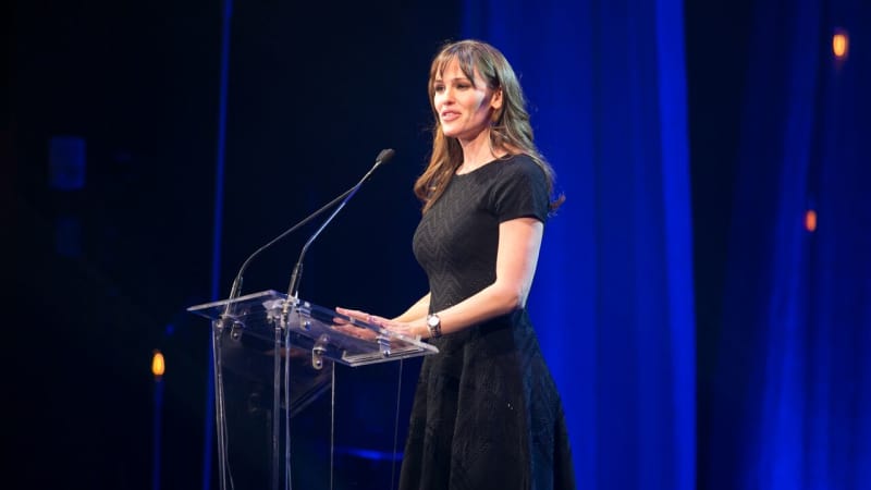 Jennifer Gardner stands and speaks at a glass podium on stage.