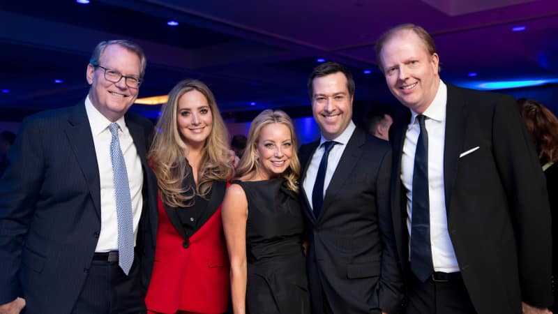 A group of five people in formal attire pose for a photo together.