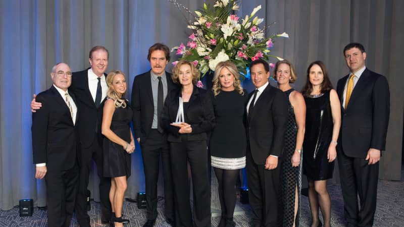 A group of ten people in formal attire pose in front of a large floral boquet.