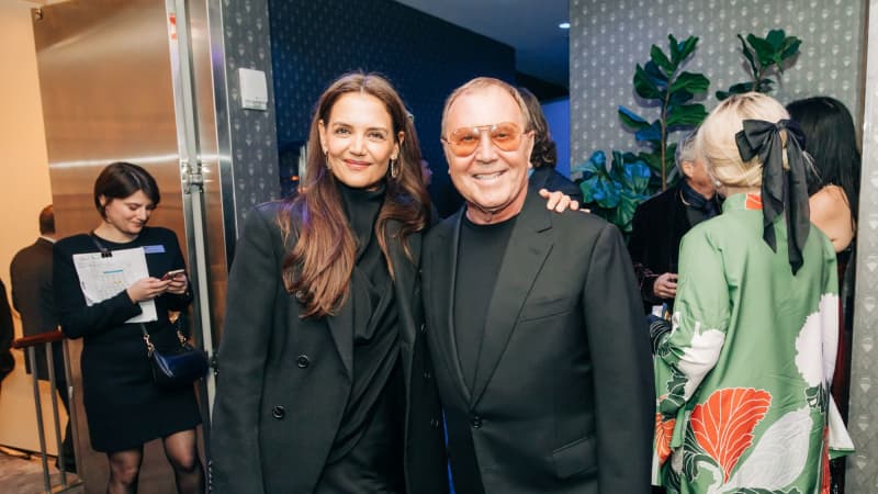 Katie Holmes and Michael Korrs both dressed in black with their arms around each other smiling for the camera. 