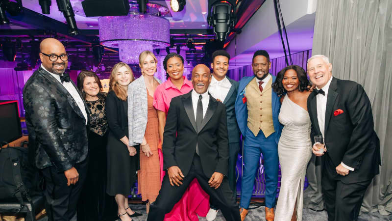 A group of adults all dressed in formal attire looking at the camera and smiling wide. 