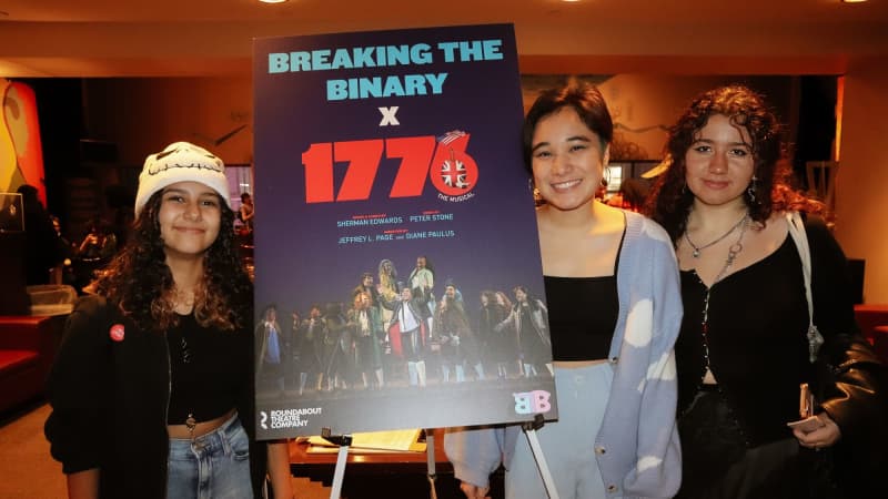 Three young adults smile and stand around a sign on a easel that says BREAKING THE BINARY X 1776.