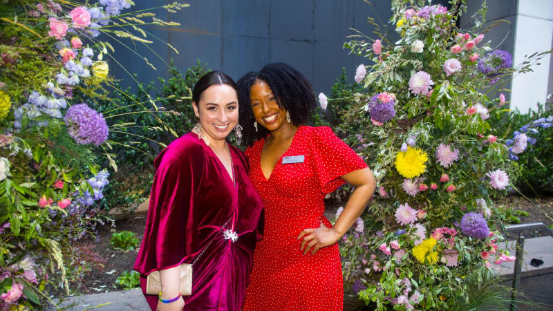Two women pose together next to large floral arrangements outside the theater.