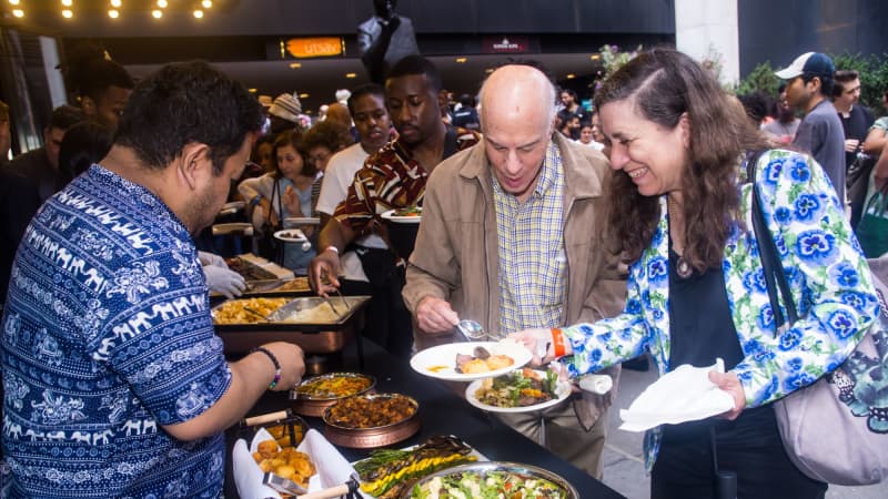 People line up by a buffet outside the theatre and fill their plates with food.