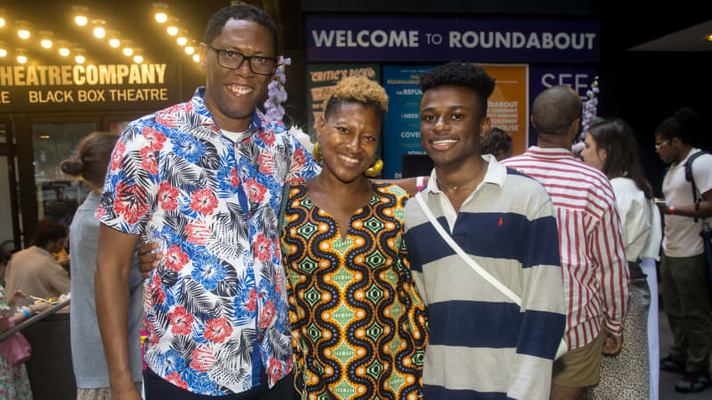 Three people stand with their arms around each other and smile for a photo outside the theater.