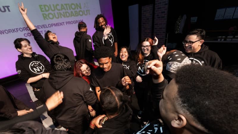 A group of TWDP students in black hoodies cheer and jump around in a clump.