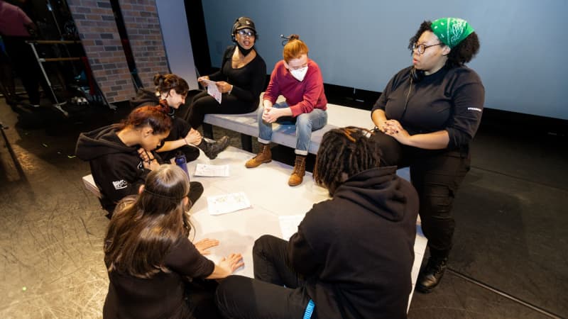 A group of students dressed in black gather on a white platform and review a schedule.