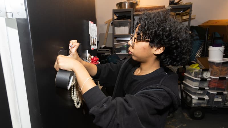 A student dressed in black rips off a piece of gaff tape backstage.