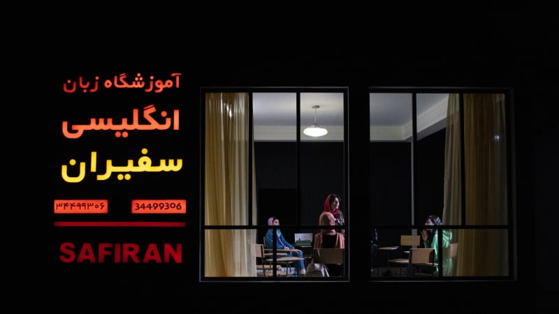 The set is turned so we see an Iranian classroom through a window. On the outside of the building is neon farsi lettering and the word SAFRIAN.