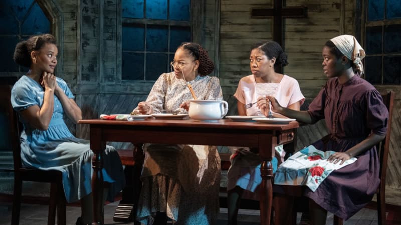 Four dark skinned woman dressed in clothing froms the 30s sitting at a table eating dinner. 