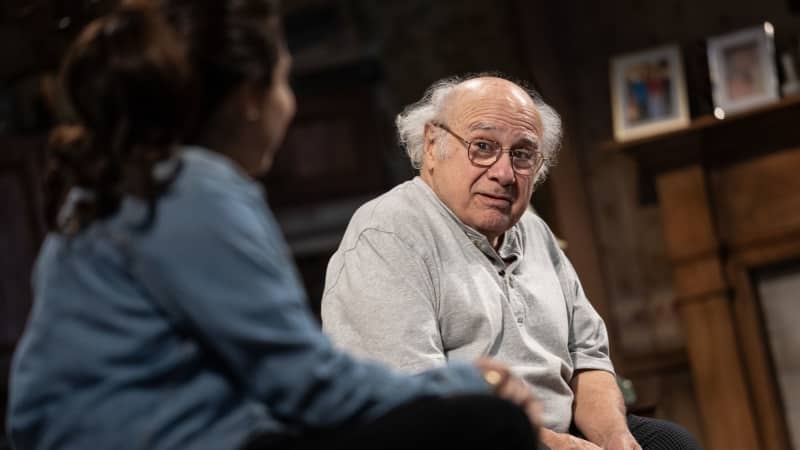 An old man with glasses sits on a couch with his daughter for a heart-to-heart conversation.