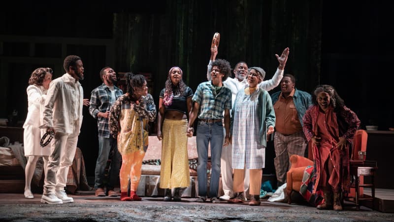 A Black family of various generations smiles, cheers, and joyously dances together on stage.