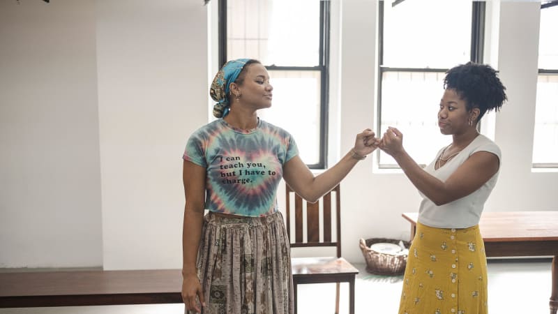 Two young black women in rehearsal doing a pinky promise with each other.