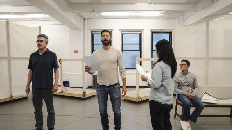 Four actors stand and sit around a rehearsal studio with scripts in hand. 