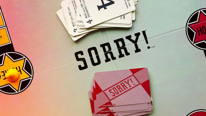 A board game with red, yellow, blue, and green paths on it. Two stacks of cards sit near the center. The word “Sorry!” is on the center of the board.